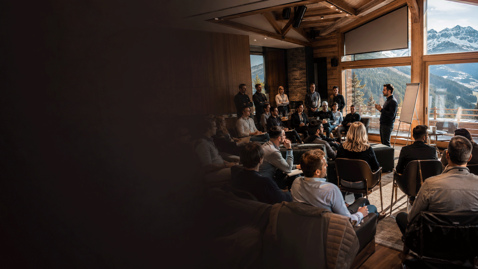 Séminaire d'entreprise dans un chalet alpin : participants attentifs face à un intervenant, baie vitrée ouverte sur les montagnes